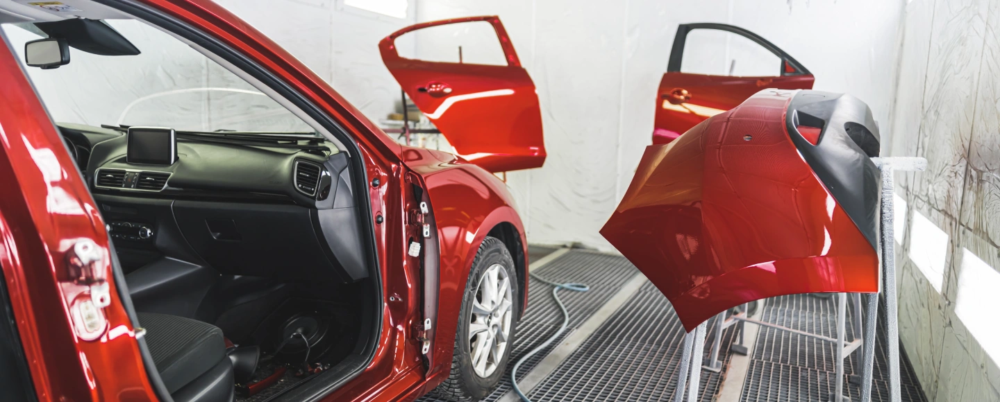 a red car is being painted inside a garage showcasing the process of automotive refinishing